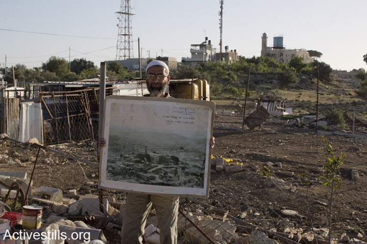 עיד ברקאת, תושב נבי סמואל, עומד מול המסגד עם תמונה של כפרו שנהרס כשהיה בן 7. צילום: מרייקה לאוקן וקרן מנור / אקטיבסטילס