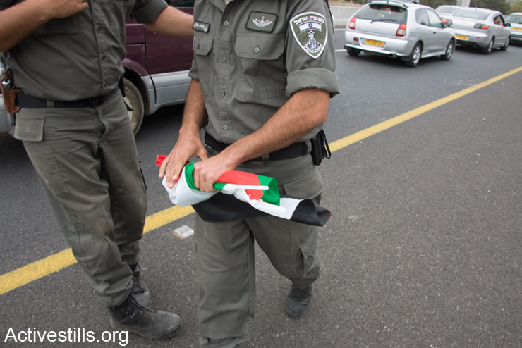שוטר מג"ב מחזיק בדגל פלסטין שהחרים מאישה פלסטינית, אזרחית ישראל, שנופפה בו בדרכה לצעדת השיבה בכפר לוביה. ה-6 למאי, 2014. לוביה הוא אחד מ- 500 הכפרים הפלסטינים שנהרסו בנכבה. (אקטיבסטילס)