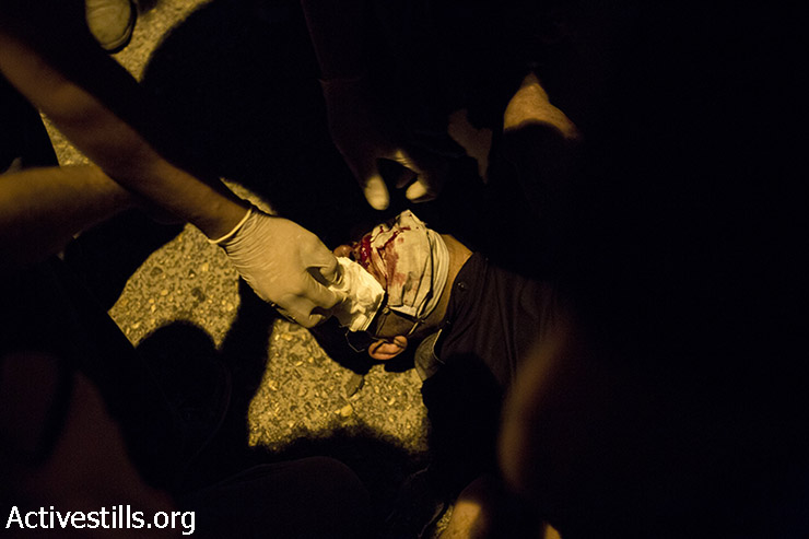 חובש פלסטיני מטפל בצעיר שנפצע במהלך עימותים בעקבות התקיפה הישראלית על רצועת עזה. מחסום קלנדיה הסמוך לרמאללה 24 ביולי 2014. (אורן זיו/ אקטיבסטילס)