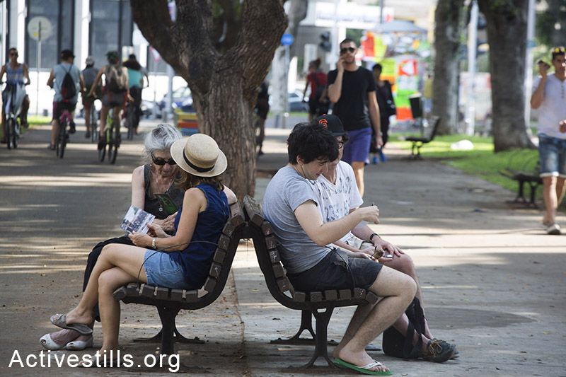 עוברים ושבים מסתכלים בגלויות שחילקו פעילי שמאל הנותנים מידע על המתקפה הישראלית בעזה, תל אביב, ה-22 ליולי, 2014. (קרן מנור/אקטיבסטילס)