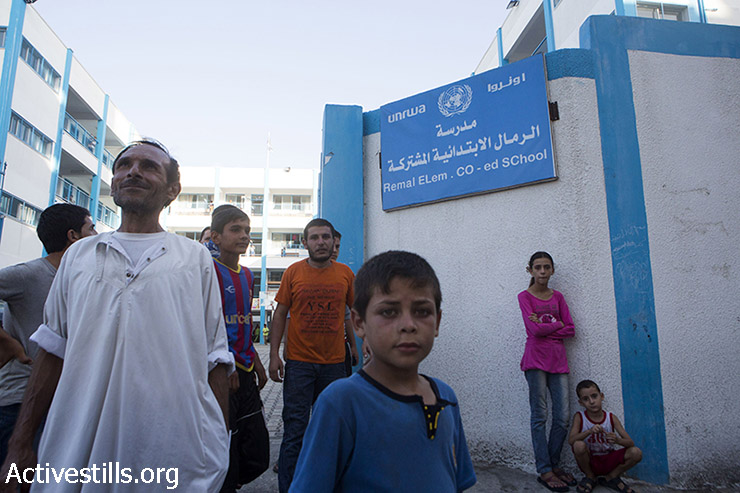 פלסטינים עומדים מול הכניסה של "בית הספר היסודי רמל" של אונר"א המשמש מקלט זמני לפלסטינים המתגוררים בחלק הצפוני של רצועת עזה, ה- 13 ביולי 2014. (אן פאק / אקטיבסטילס)