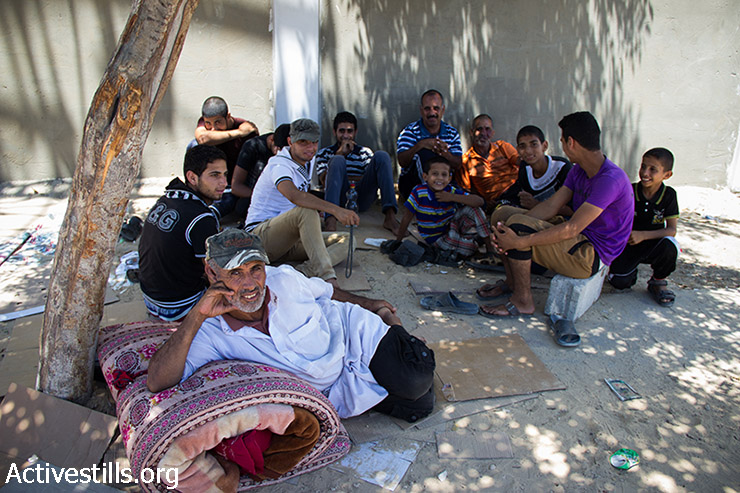 משפחה פלסטינית מעבסאן יושבת מתחת לעץ ליד בית החולים בחאן יונס. זהוא יומה העשירי של המשפחה תחת העץ, אחרי שנאלצו לברוח מביתם בשל התקיפה הישראלית. רצועת עזה, 24 ביולי 2014. (באסל יאזורי / אקטיבסטילס)
