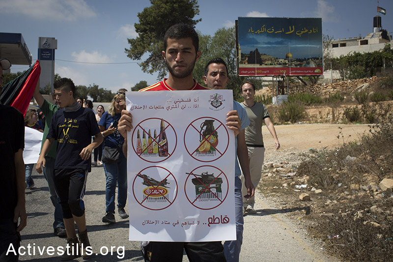 פלסטיני מחזיק שלט הקורא להחרים מוצרים ישראליים בשטחי הגדה המערבית, במהלך הפגנה נגד הכיבוש בכפר נבי סלאח, הגדה המערבית, ה 22 לאוגוסט, 2014. (אורן זיו/אקטיבסטילס)