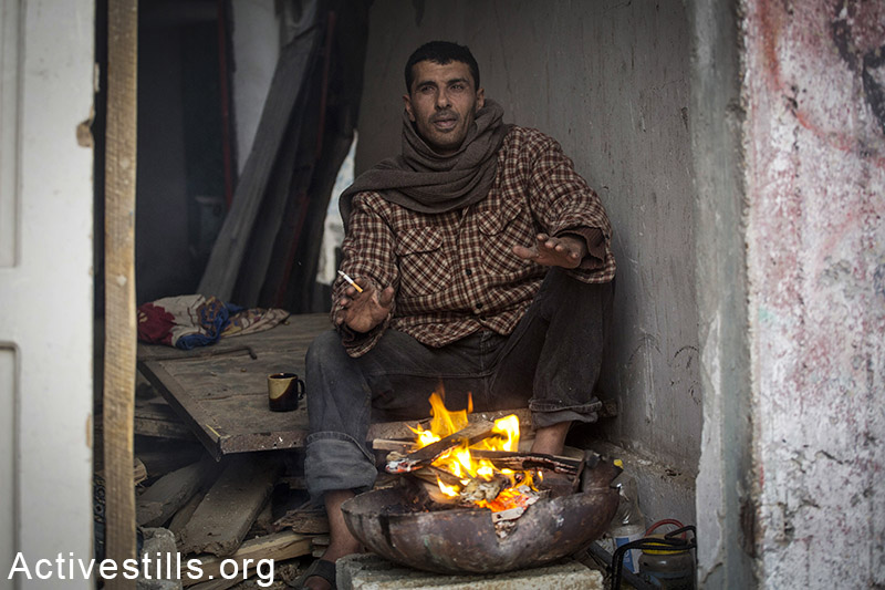 פלסטיני מנסה להתחמם בחורבות ביתו, שכונת שג׳עיה, רצועת עזה, 11 פברואר, 2015. אן פאק / אקטיבסטילס