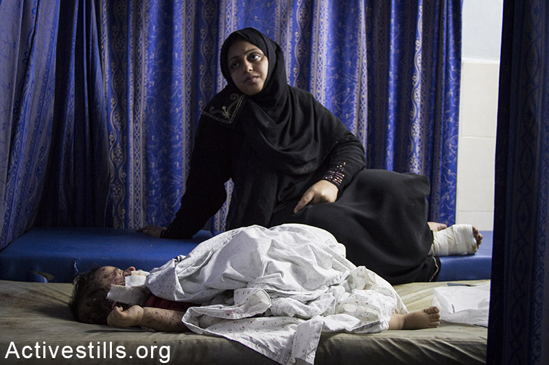 אישה מחכה לטיפול בילדה הפצוע לאחר הפגזה ישראלית, בבית החולים אל-שיפא, עזה, 30 יולי, 2014. באסל יאזורי / אקטיבסטילס