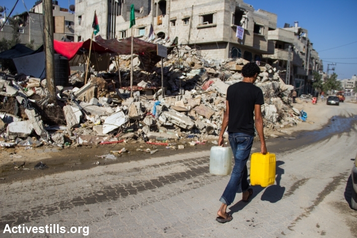 תושב שכונת שג'אעיה סוחב מיכלי מים, ספטמבר 2014 (באסל יאזורי / אקטיבסטילס)