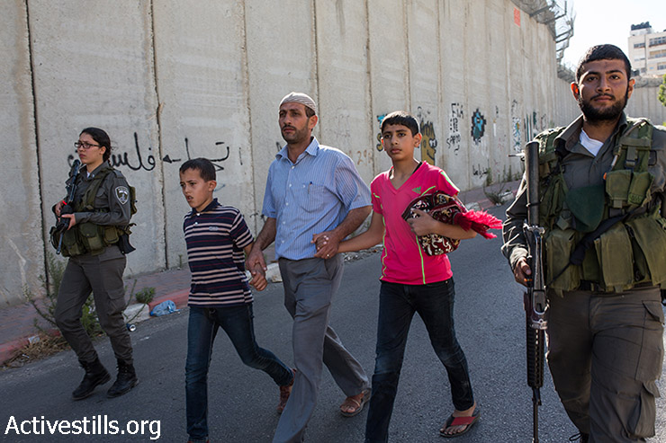 שוטרי מג״ב עוצרים פלסטינים לאחר שניתפסו מטפסים על חומת ההפרדה על מנת להשתתף בתפילות יום השישי השני של חודש הרמאדן במסגד אל-אקצא, בעיירה אל-ראם, ליד מחסום קלנדיה בין רמאללה וירושלים, 3 ביולי 2015. (יותם רונן/אקטיבסטילס)