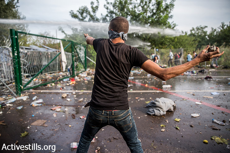 פליט זורק אבנים על שוטרים הנגרים במהלך מחאת פליטים מול הגבול הסגור, בצד הסרבי של גבול סרביה-הונגריה, 16 בספטמבר 2015. (יותם רונן/אקטיבסטילס)