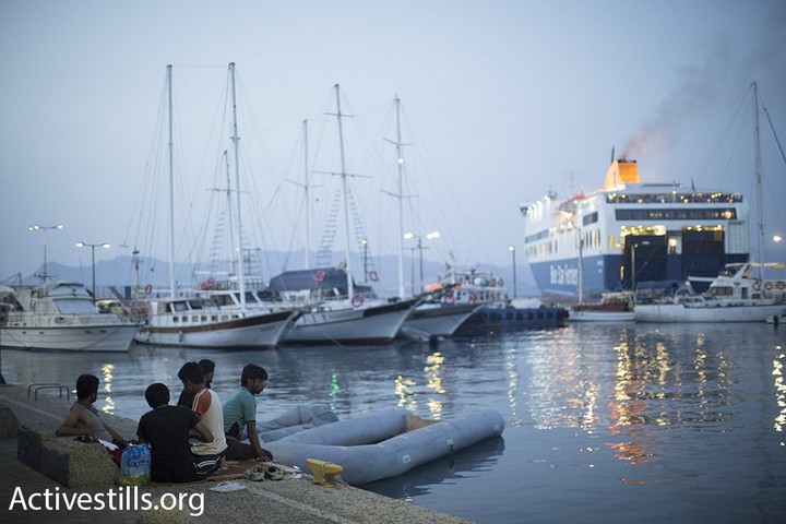 פליטים אפגנים יושבים בנמל של קוס ומביטים על מעבורת מלאה בפליטים סורים ותיריים בדרכם לאתונה. (אורן זיו/אקטיבסטילס)