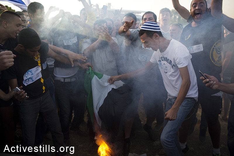 פעילי ימין שורפים דגל פלסטין וקוראים קריאות גזעניות במהלך הפגנה בצומת גוש עציון בעקבות חטיפתם של שלושה צעירים מתנחלים ארבעה ימים קודם לכן. 16 ביוני, 2014. (אורן זיו/אקטיבסטילס)