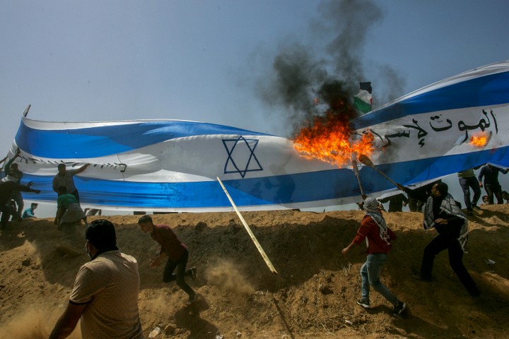 פלסטינים שורפים דגל ישראל בצעדת השיבה בגבול עזה. 6 באפריל 2018 (עבד רחים ח'טיב / פלאש90)