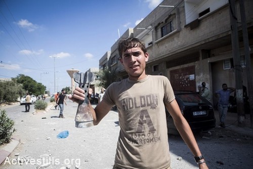 תושב עזה מציג חתיכה מטיל ישראלי בכפר עבאסן. 26 ביולי, 2014. (אן פאק / אקטיבסטילס)
