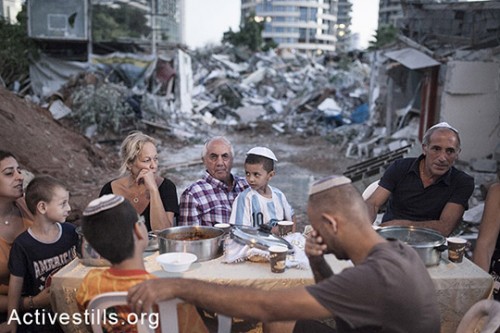משפחת חליף יושבת לשולחן שבת ומאחוריהם חורבות ביתם שנהרס על ידי חברות פרטיות לאחר פינויים, גבעת עמל, ה-19 בספטמבר, 2014. (שירז גרינבאום/אקטיבסטילס)