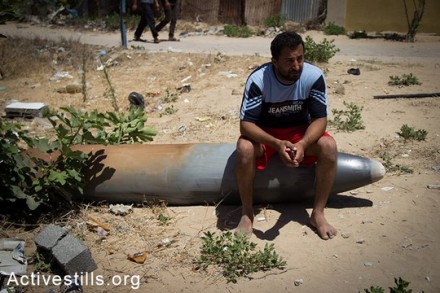 חאסן שאמדי יושב על טיל ישראלי שלא התפוצץ לאחר תקיפה ישראלית שהרסה את ביתו יום קודם לכן, בשכונה תל אל-האווה בעיר עזה, ה-14 ליולי, 2014. (אן פאק/אקטיבסטילס)