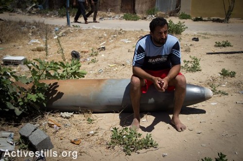 חאסן שאמדי יושב על טיל ישראלי שלא התפוצץ לאחר תקיפה ישראלית שהרסה את ביתו יום קודם לכן, בשכונה תל אל-האווה בעיר עזה, ה-14 ליולי, 2014. (אן פאק/אקטיבסטילס)
