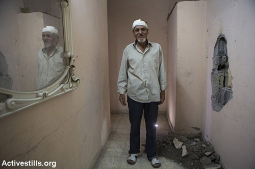 מג'יד אל-זים, בן 52, עומד בביתו ההרוס. בקיר הימני ניתן לראות חור שנגרם מפגיעת טיל ששוגר לעבר הבית ממזל״ט צבאי, ואשר גרם גם לפציעתו של אל-זים, עזה, 14 ביולי 2014. הטיל שוגר כאזהרה לפני תקיפה אווירית על על בית סמוך, נוהל הידוע גם בכינוי ״הקש בגג״. (אן פאק/אקטיבסטילס)