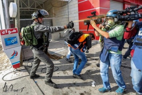 שוטר מג"ב מרסס עיתונאים וחובשים בגז פלפל, צומת בית אל 30 באוקטובר 2015. החובש אחמד נאסר בווסט הכתום נראה מתכופף (פאדי ערורי)