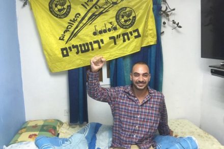 דוד מזרחי בביתו עם דגל בית"ר מעל המיטה (מיכאל סולסברי-כורך)