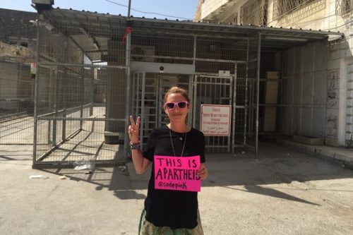אריאל גולד על רקע מחסום בחברון. על השלט הוורוד שהיא אוחזת כתוב "זהו אפרטהייד" (צילום באדיבות המצולמת)