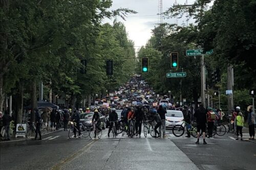 לפחות במקרה אחד, רוכבי האופניים מנעו מנהג לדהור לתוך קהל המפגינים. "בריגדת האופניים של סיאטל" על רקע הפגנה בעיר (צילום: ג'ן מרלו)