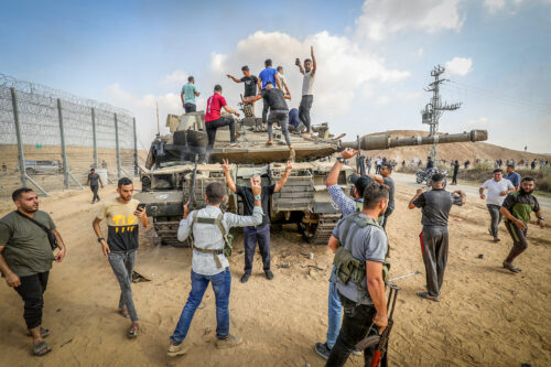 במקום לחפור תחתיה, אנשי החמאס פשוט הפילו את הגדר. פלסטינים סביב טנק ישראל צמוד לגדר שנפרצה, 7 באוקטובר 2023 (צילום: עבד רחים ח'טיב / פלאש 90)