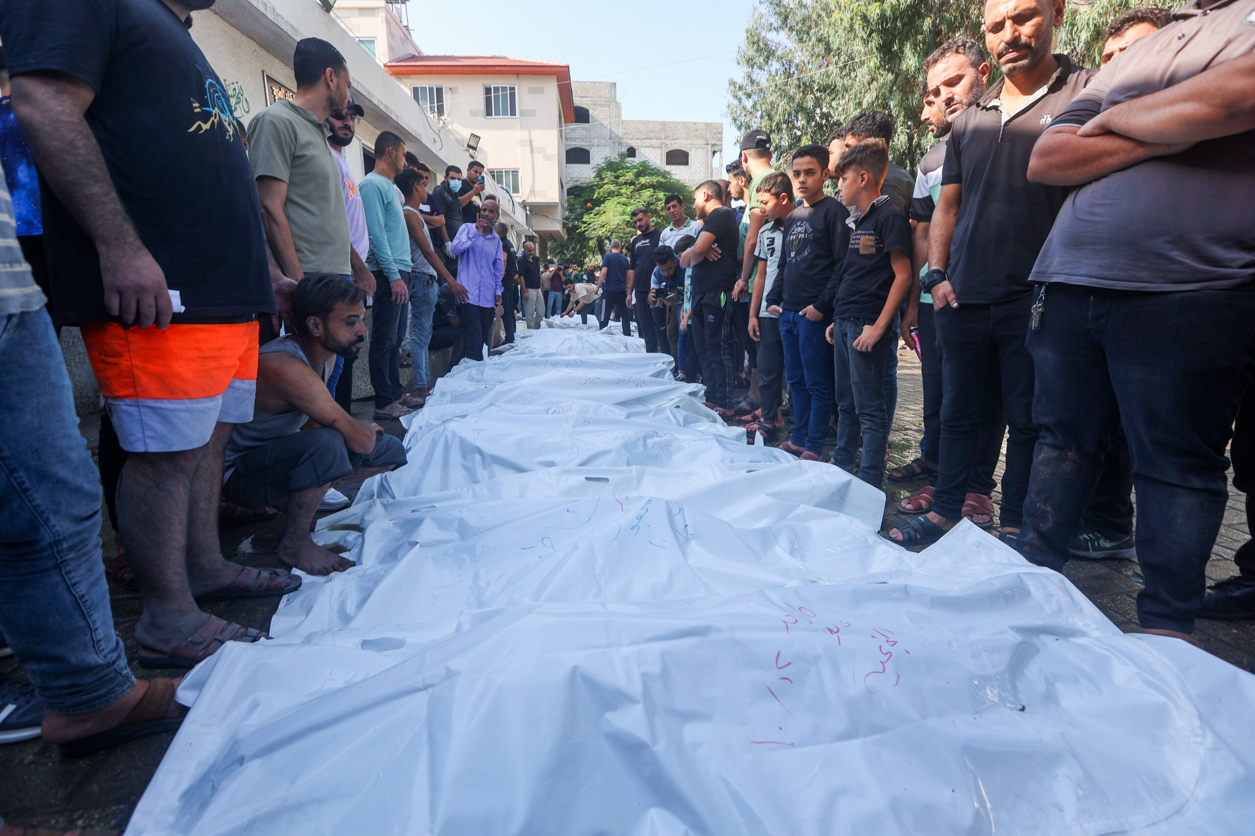 פלסטינים עומדים מעל גופות של הרוגים בהפצצה אווירית ישראלית, מחוץ לבית החולים שיפא בעיר עזה, ב-12 באוקטובר 2023 (צילום: עטיה מוחמד / פלאש90)