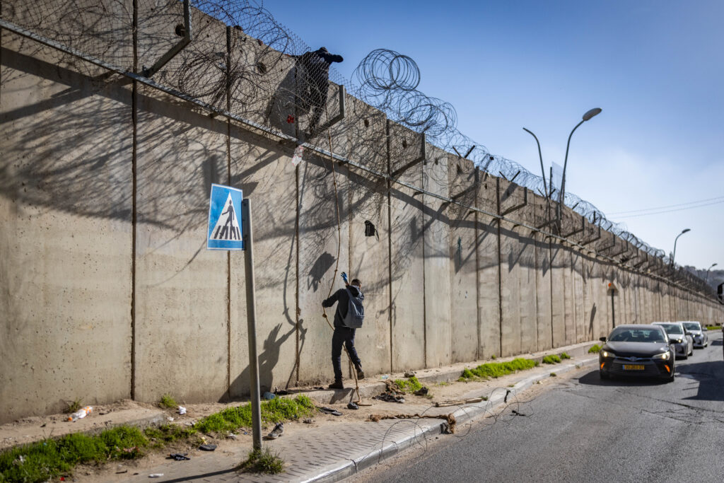 פלסטינים מטפסים על גדר ההפרדה בניסיון להשיג עבודה בישראל, בדצמבר 2025 (צילום: חיים גולדברג / פלאש90)